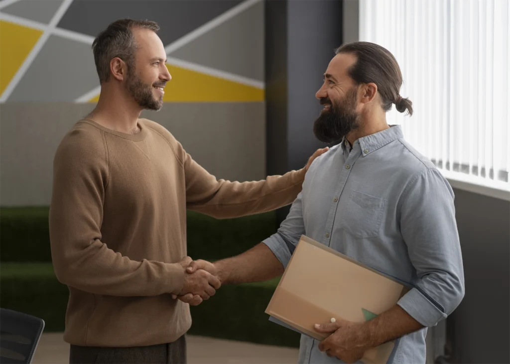 An image of two businessmen men in a modern office. They are standing and shaking hands.