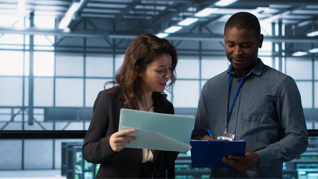 Two well dressed professionals standing in a glass building reviewing reports